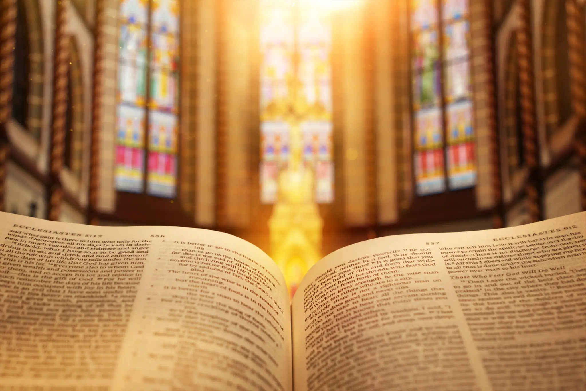 Open Bible with sunlight streaming through stained glass windows.